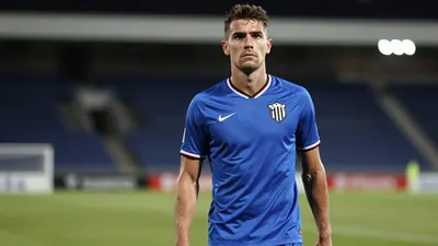 Muscular defender in a solid blue jersey, standing confidently on a football pitch with a determined expression