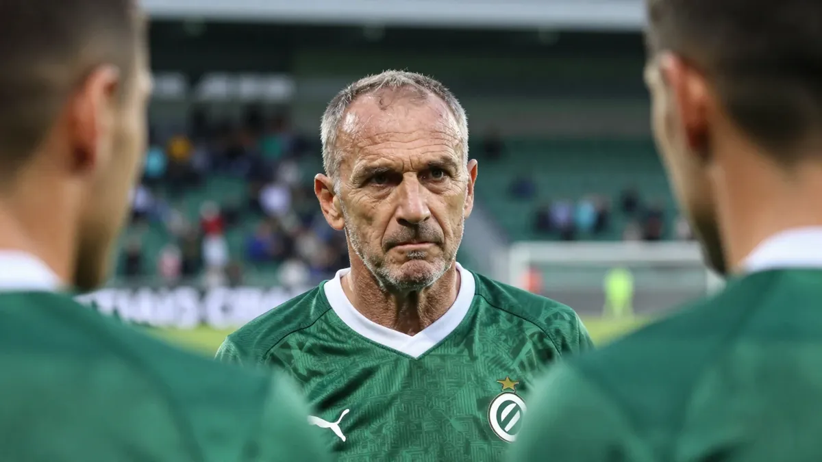 A close-up shot of a middle-aged, ruggedly-built, unshaven head coach in his late 50s, with a stern expression, gazing...