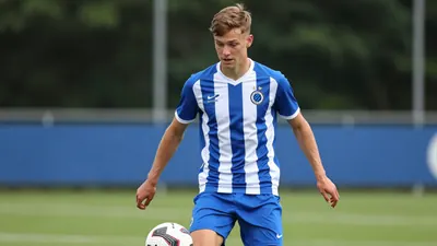 A photorealistic image of a 21-year-old anonymous left winger wearing a Cercle Brugge jersey (blue and white striped...