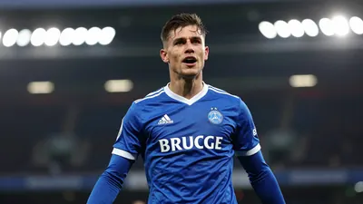 Photorealistic image of a Cercle Brugge player in a blue jersey celebrating a goal, blurred stadium background