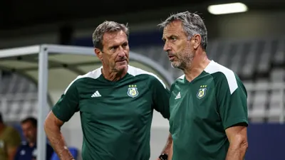 A 45-year-old male coach, with a rugged complexion and graying temples, stands in the Jan Breydelstadion's tunnel, his...