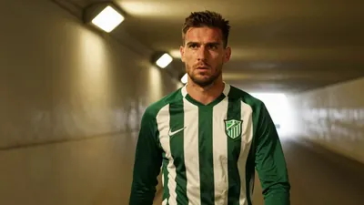 A 35-year-old, ruggedly-built, central defender with a weathered complexion, dressed in a dark green and white striped...
